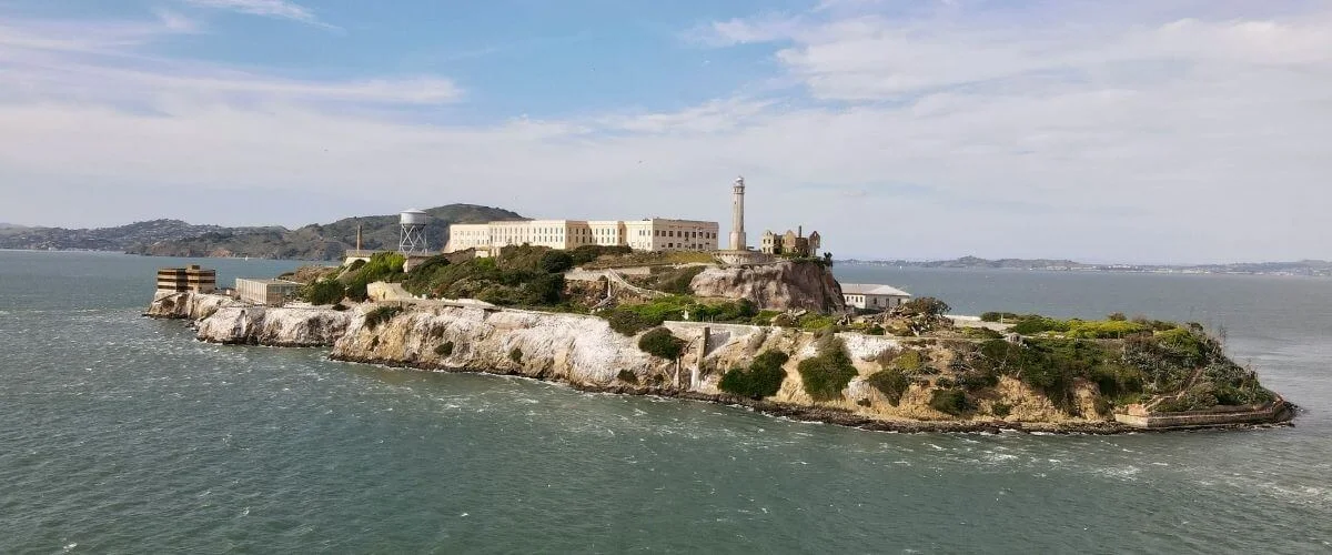 Alcatraz Island with Lighthouse in San Francisco Bay A panoramic view of Alcatraz Island featuring historic prison buildings and a lighthouse, surrounded by water in San Francisco Bay under a clear sky.
