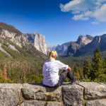person sitting on a rocky ledge looking out at yosemite
