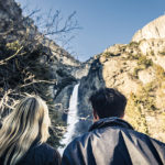 two people looking up at a waterfall