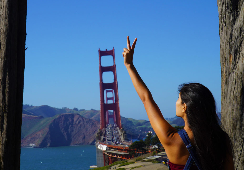 person holding a peace sign in front of golden gate bridge