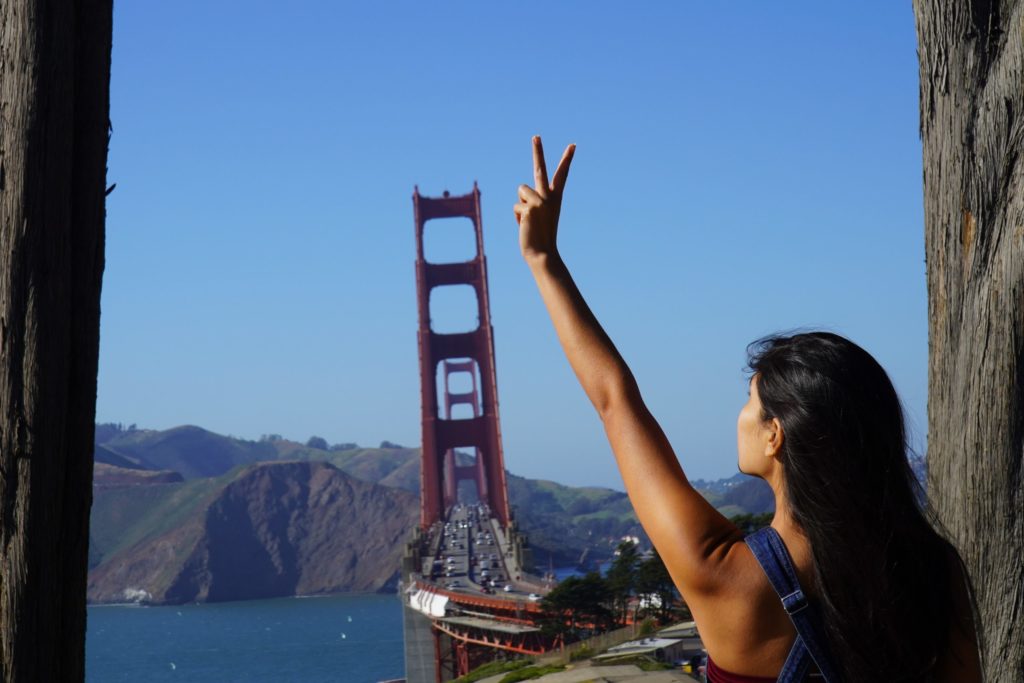 person holding up a peace sign with the golden gate in the background
