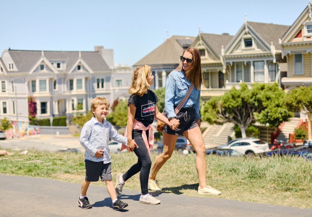 Woman and children walking hand-in-hand in Alamo Square in front of the famous Painted Ladies