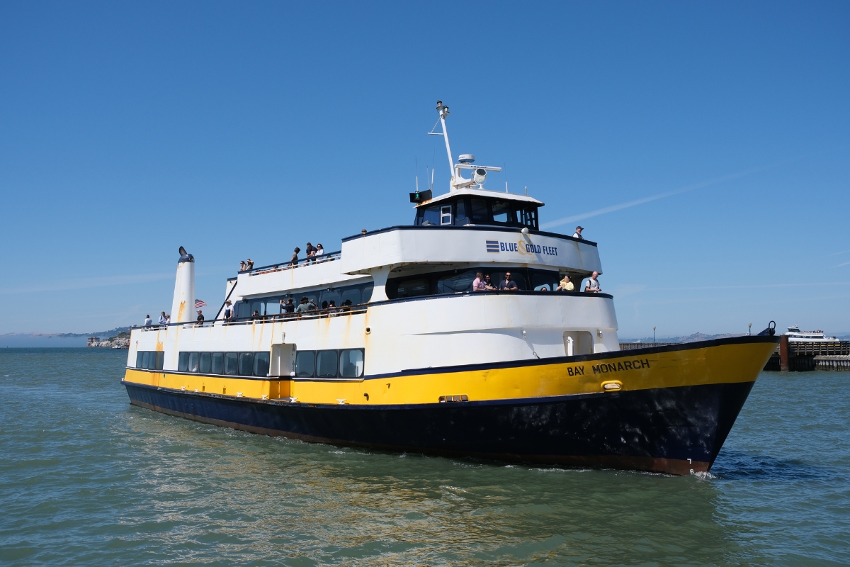 White and yellow Blue & Gold Fleet ferry boat named Bay Monarch sailing on San Francisco Bay with passengers on deck.