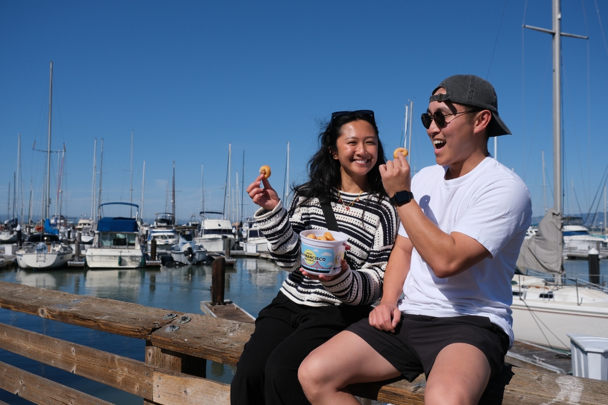 Couple eating seafood snacks at San Francisco marina with sailboats in background