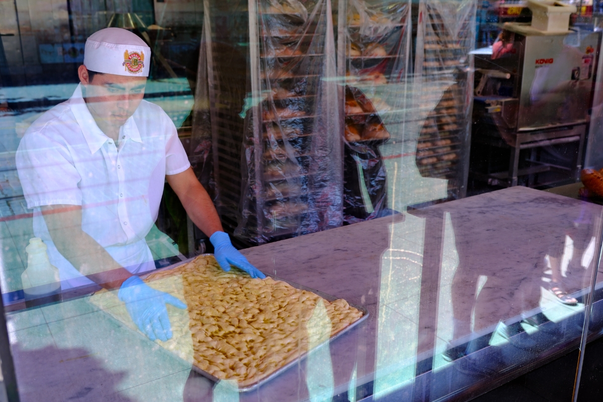 Food vendor in white uniform and gloves preparing food on a tray visible through glass window.