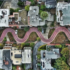 Aerial and street-level views of Lombard Street in San Francisco showing its famous zigzag brick path, flower gardens, surrounding homes, and Bay vista in perfect sunny weather conditions.