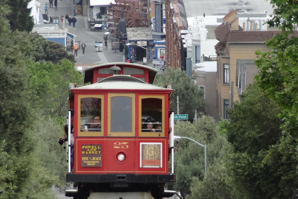 Historic red Powell-Hyde cable car #25 climbing steep San Francisco street with passengers