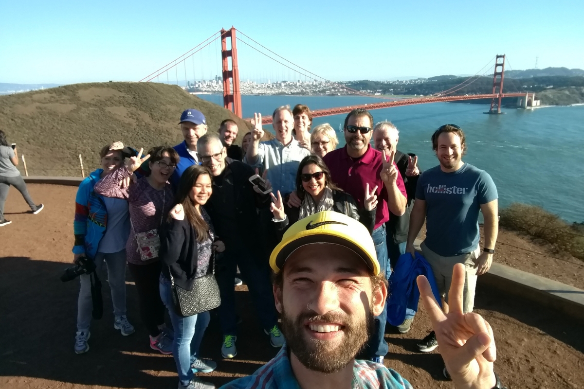 Large group photo with Golden Gate Bridge backdrop, tourists making peace signs on scenic overlook