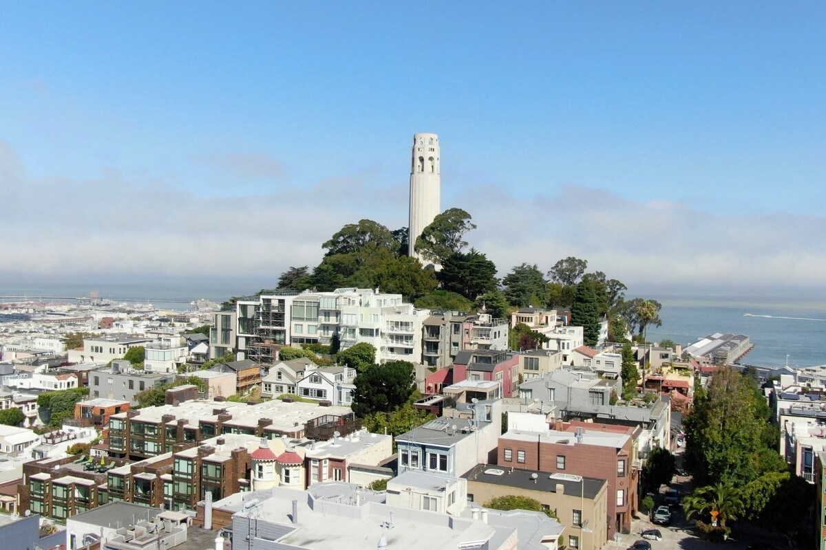 Aerial view of Coit Tower standing tall on Telegraph Hill surrounded by San Francisco residential buildings with the bay in background