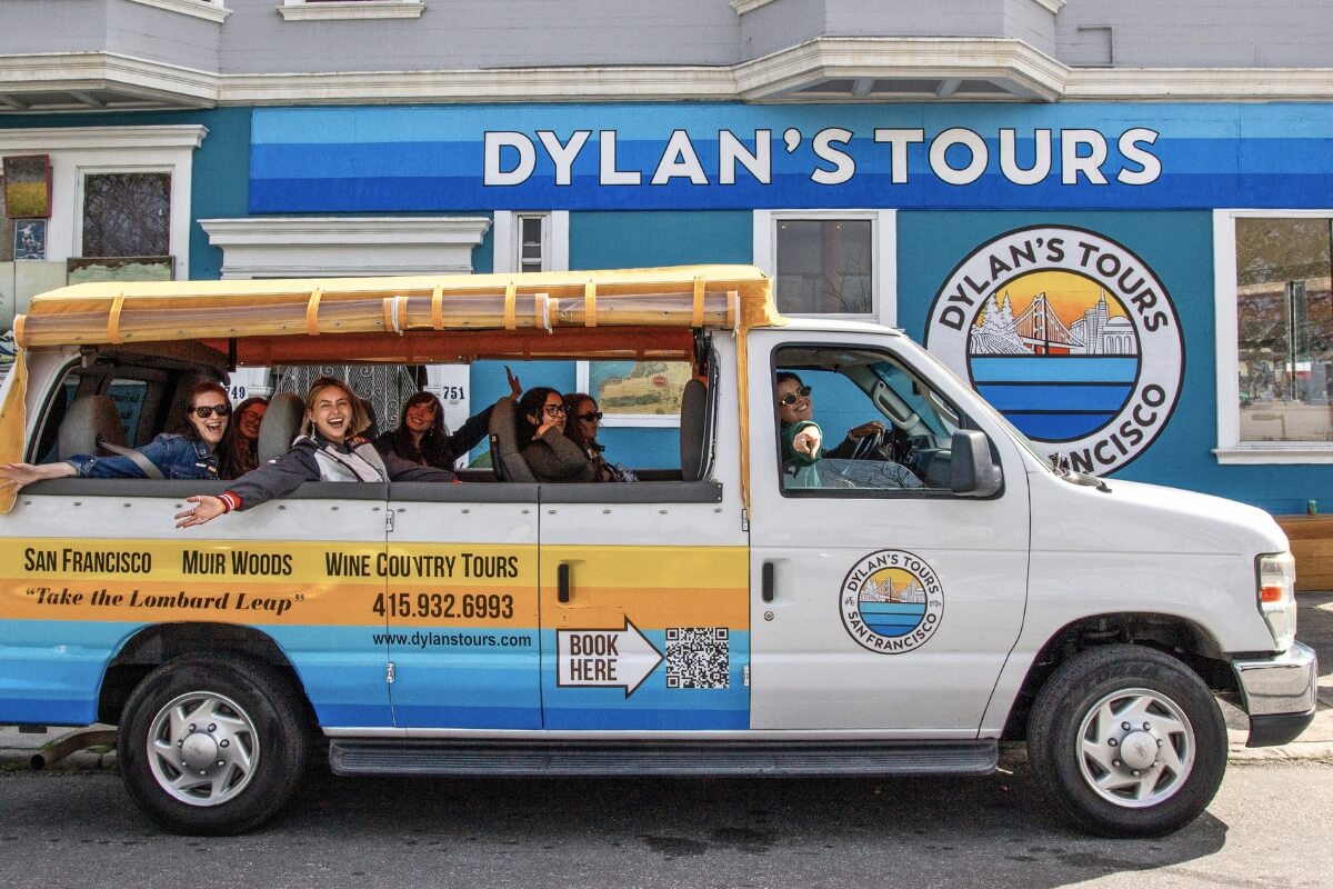 Dylan's Tours branded minibus with excited tourists waving from open-air seats in San Francisco