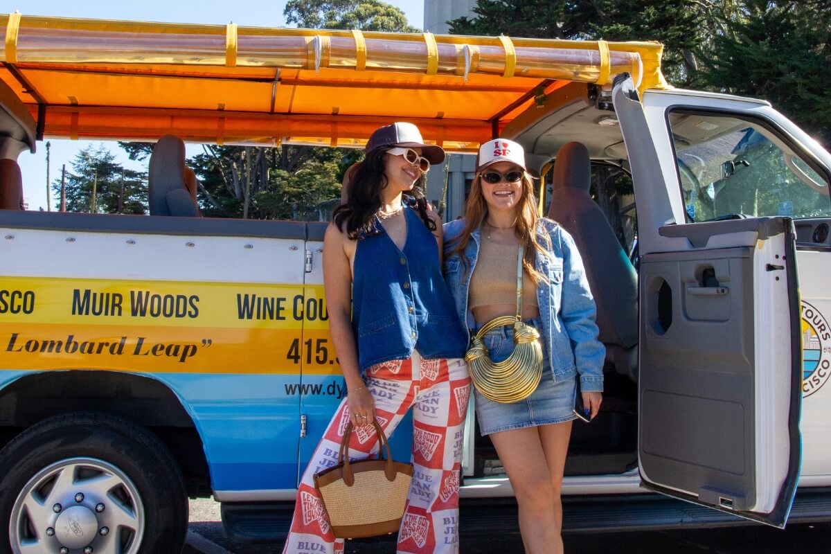 Tourists posing by Dylan's Tours van with Coit Tower visible in background