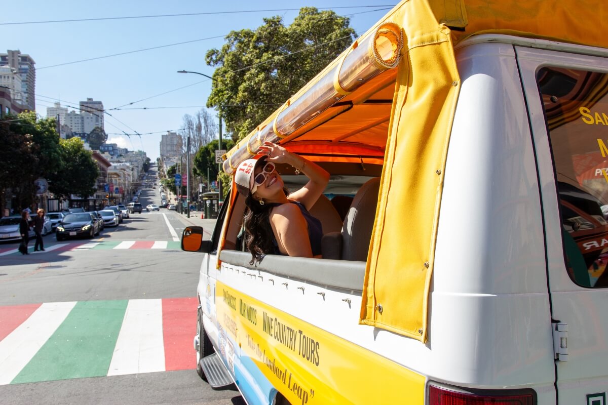 Yellow and blue tour van with "Wine Country Tours" branding driving through San Francisco's hilly streets