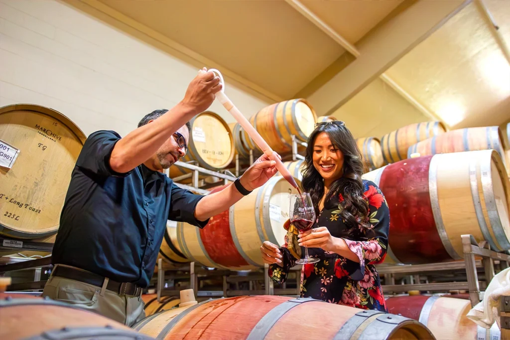 Man pouring wine from a barrel into a glass for a woman in a cozy, well-lit wine cellar, capturing a warm and personal tasting experience.