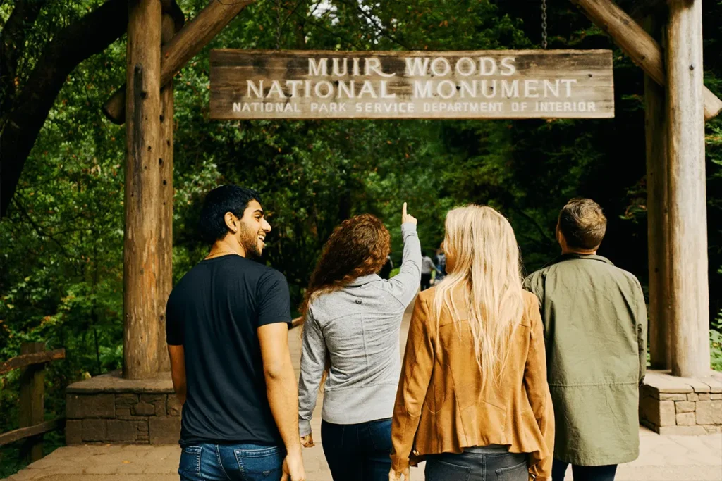 Group of friends standing at the entrance of Muir Woods National Monument surrounded by redwoods