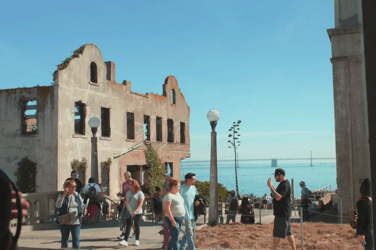 A group of tourists walking around Alcatraz Island with historic prison buildings in the background on a sunny day