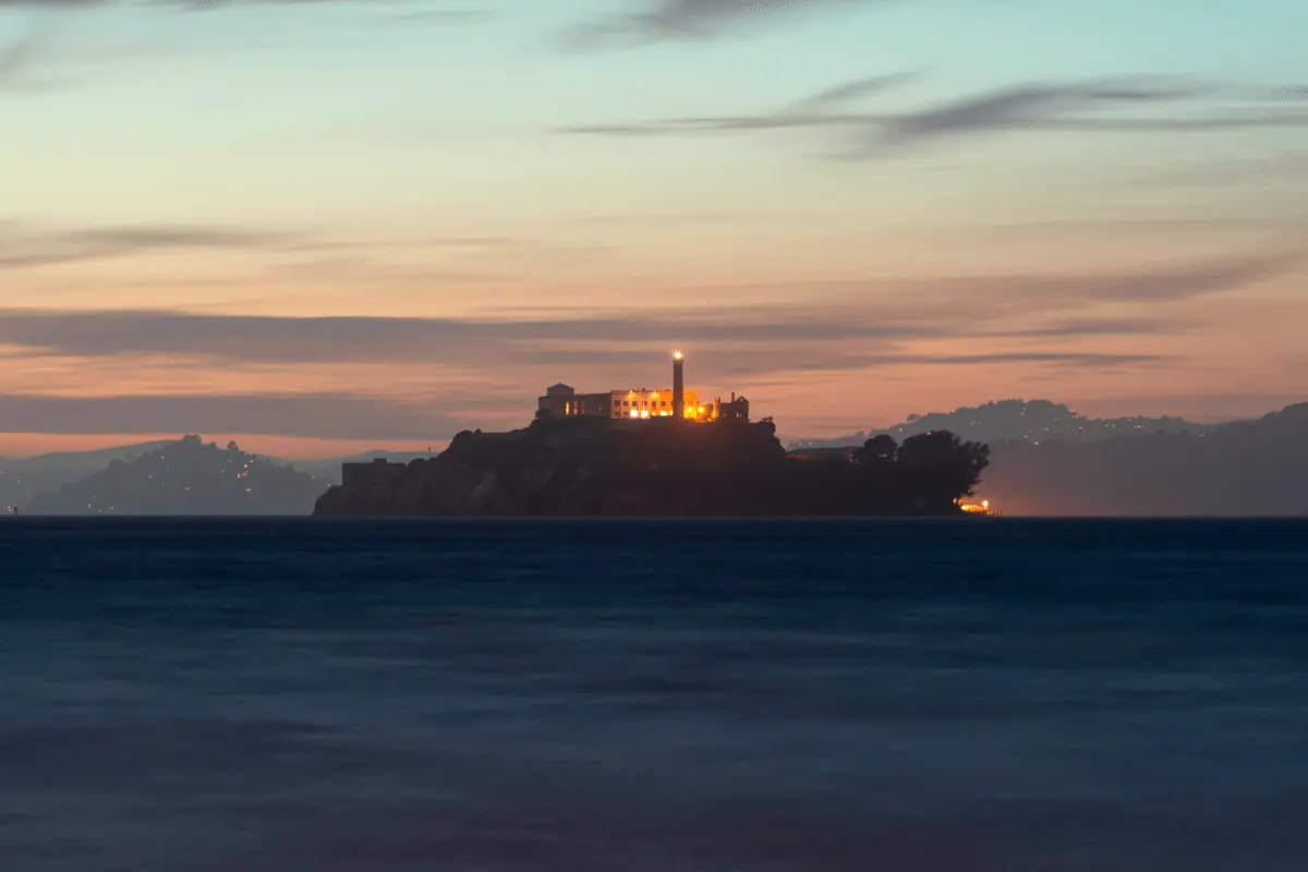 Nighttime view of Alcatraz Island surrounded by dark waters, with environmental lighting illuminating the historic prison buildings against the night sky