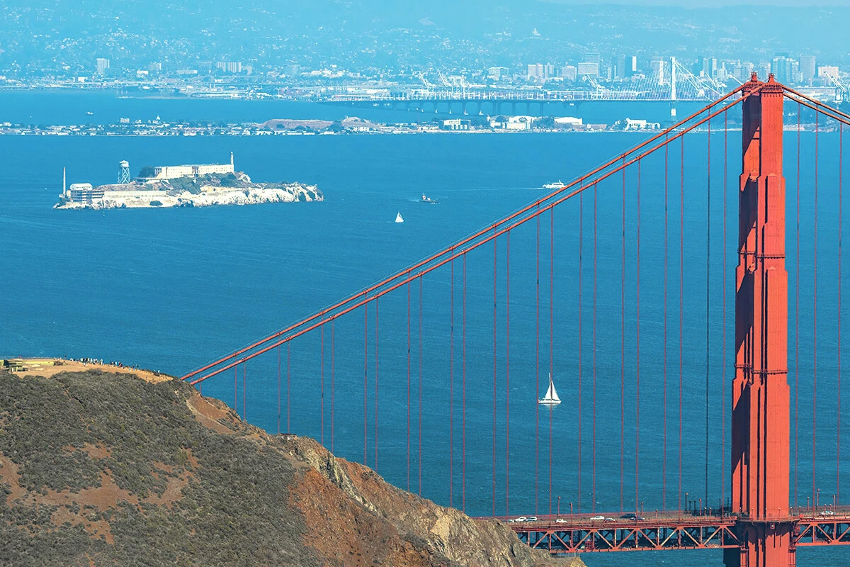 Wide view of Alcatraz Island with the Golden Gate Bridge in the distance across San Francisco Bay.