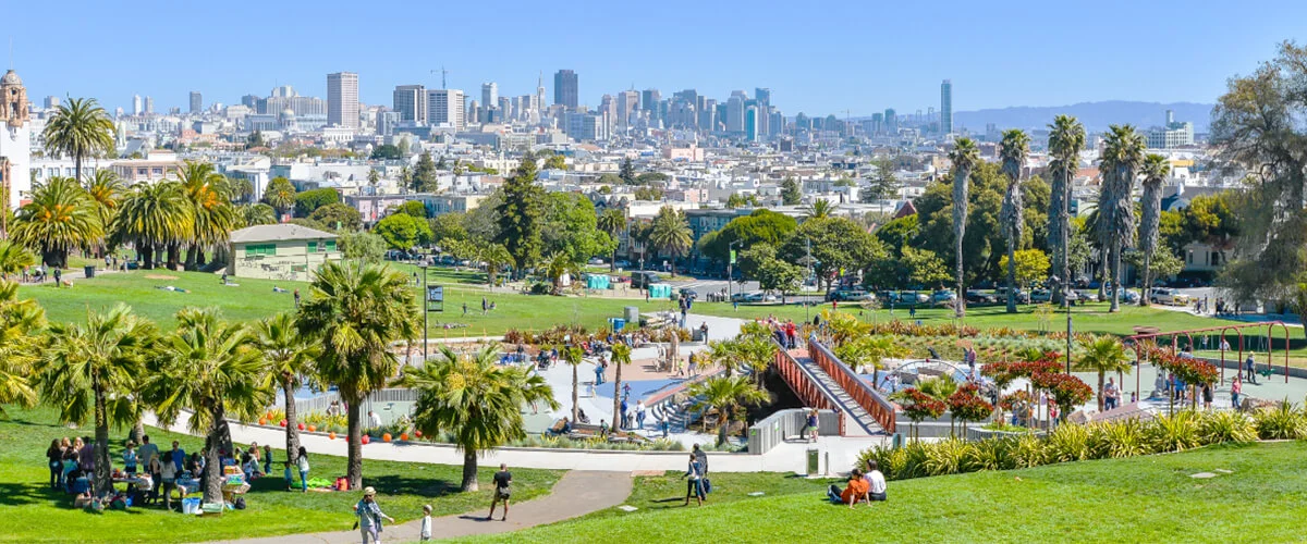 People relaxing on the grass at Dolores Park with the San Francisco skyline in the background.