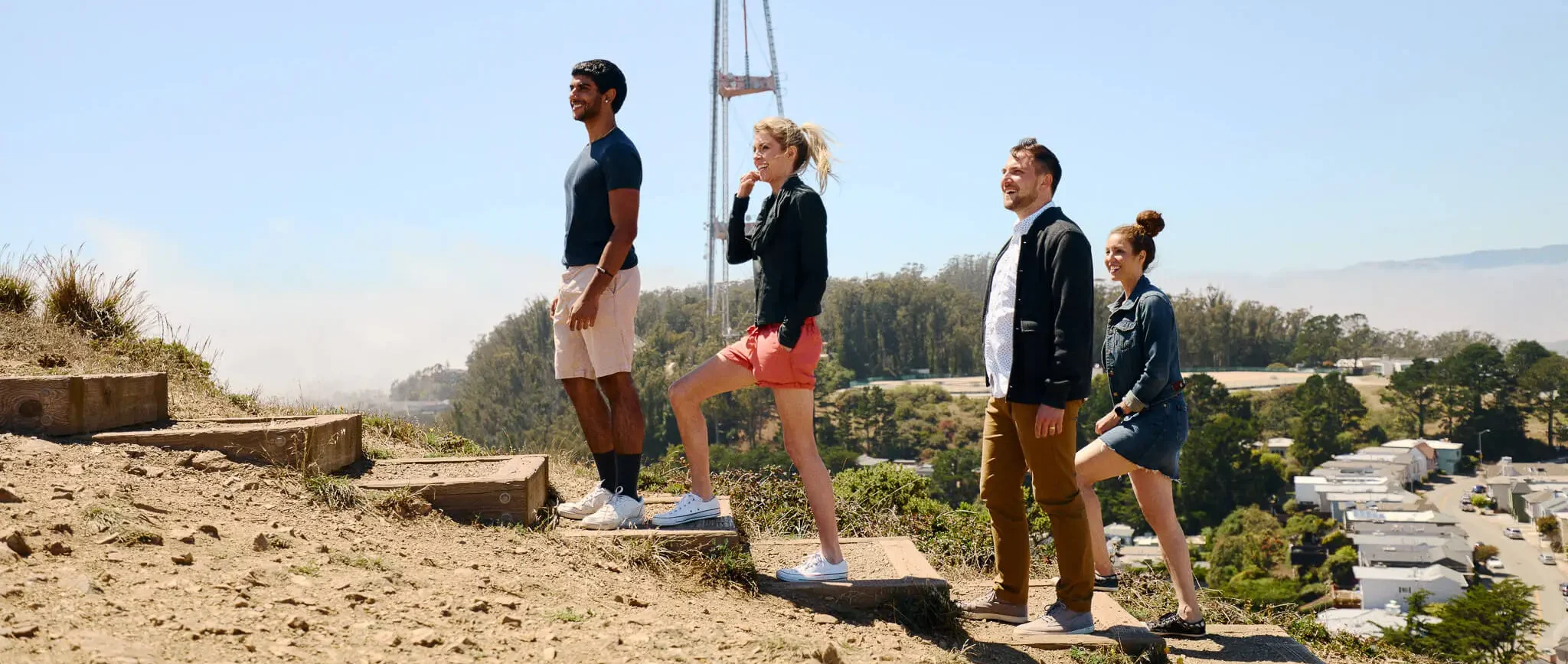 Group of friends hiking up a dirt trail with Sutro Tower rising in the background, San Francisco.