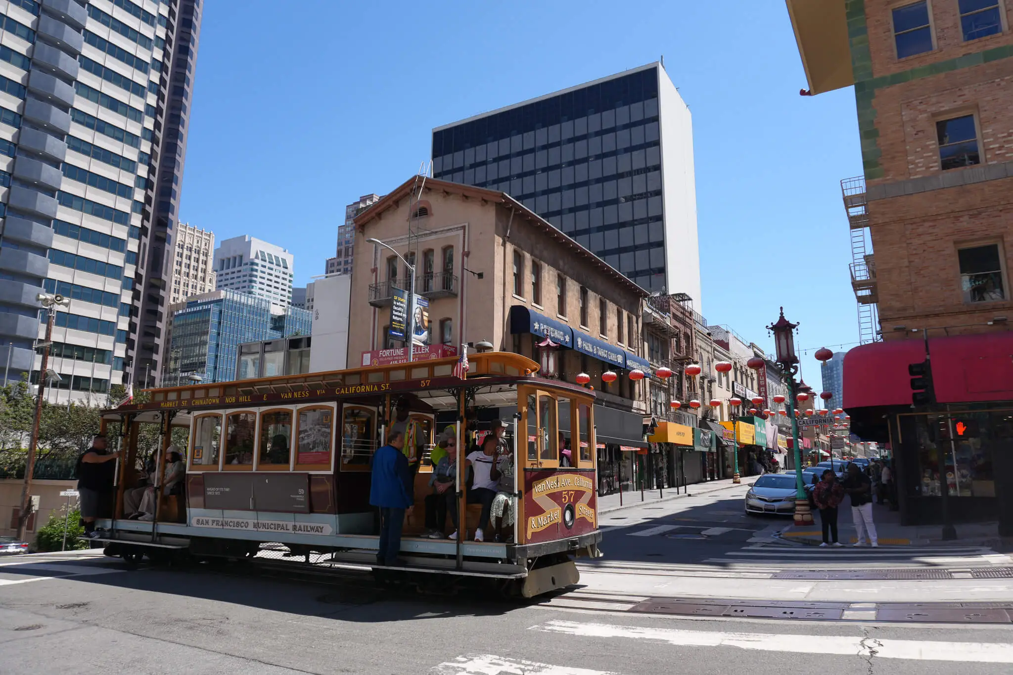 San Francisco cable car traveling through Chinatown with red lanterns hanging above the street.