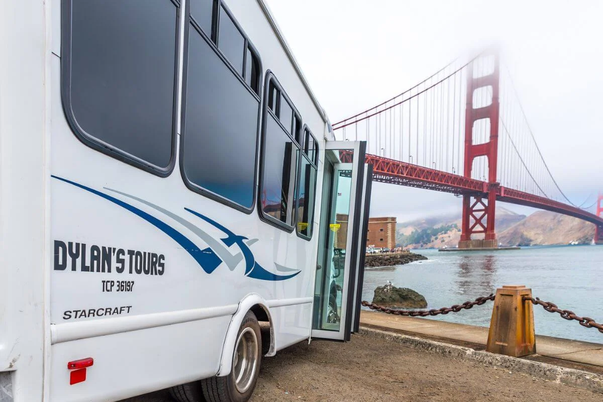 A Dylan’s Tours bus parked near the waterfront with the Golden Gate Bridge visible in the background on a foggy day in San Francisco.