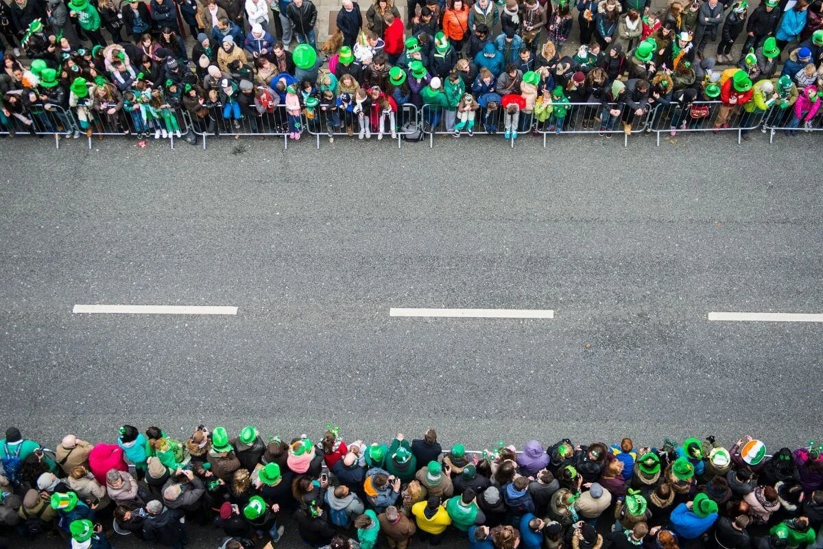 Overhead view of a large crowd wearing green gathered along a street for a St Patrick’s Day parade