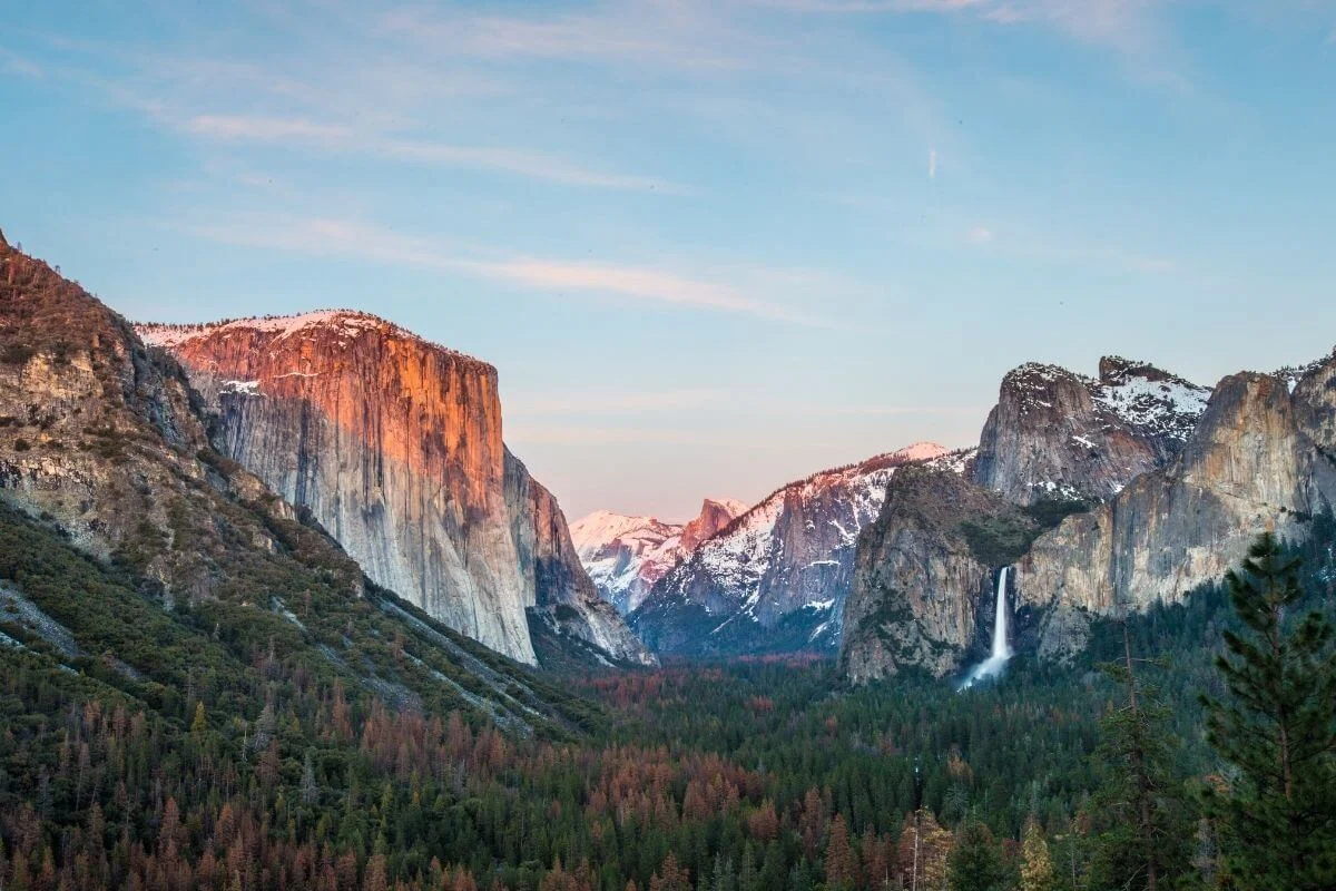 Yosemite Valley at sunset showing El Capitan, Bridalveil Fall, and forested landscape under a colorful sky
