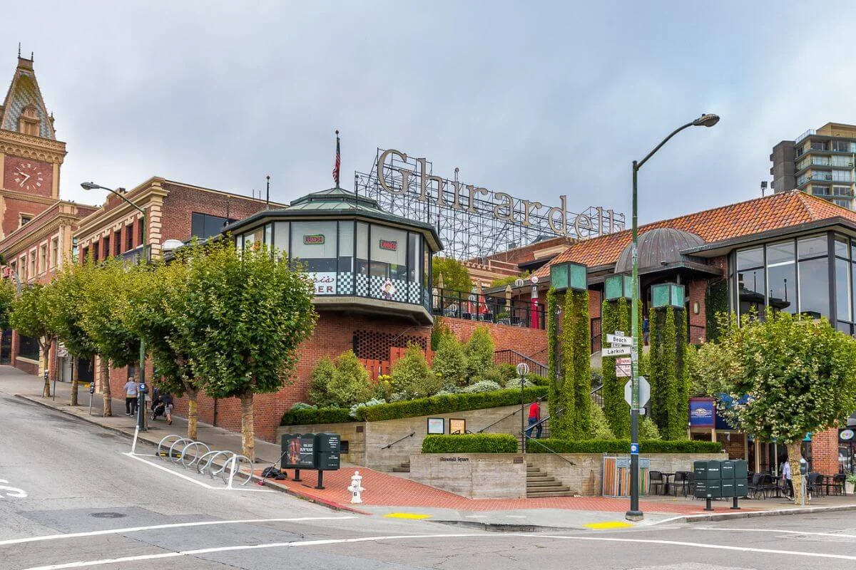 Ghirardelli Square in San Francisco with historic brick buildings, shops, greenery, and street-level views at the intersection.