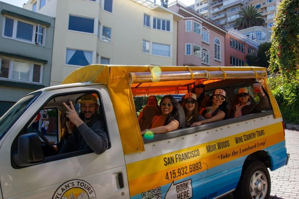 Group of tourists smiling inside an open air tour van driving through a San Francisco neighborhood