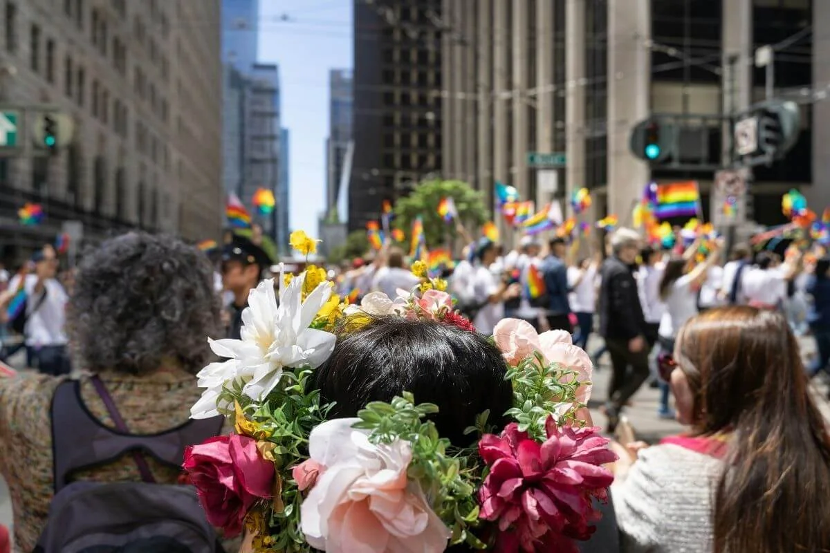Person wearing a flower crown watching the San Francisco Pride parade with rainbow flags lining a downtown street