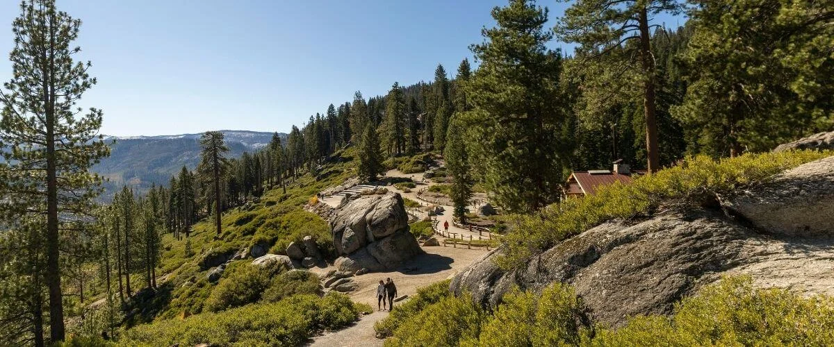 Yosemite National Park Hiking Trail and Granite Rocks Visitors walking along a hiking trail with granite rock formations and pine trees in Yosemite National Park