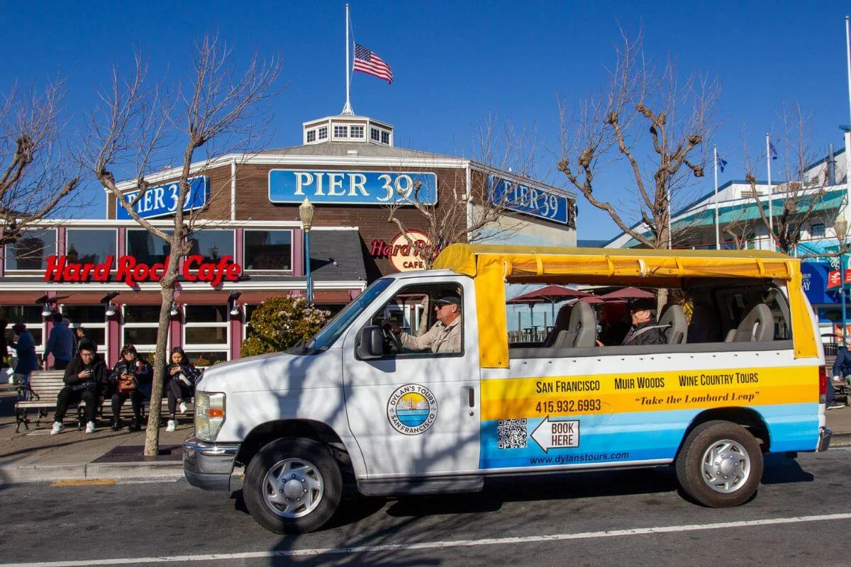 Dylan’s Tours sightseeing van parked outside Pier 39 and Hard Rock Cafe in San Francisco with visitors nearby