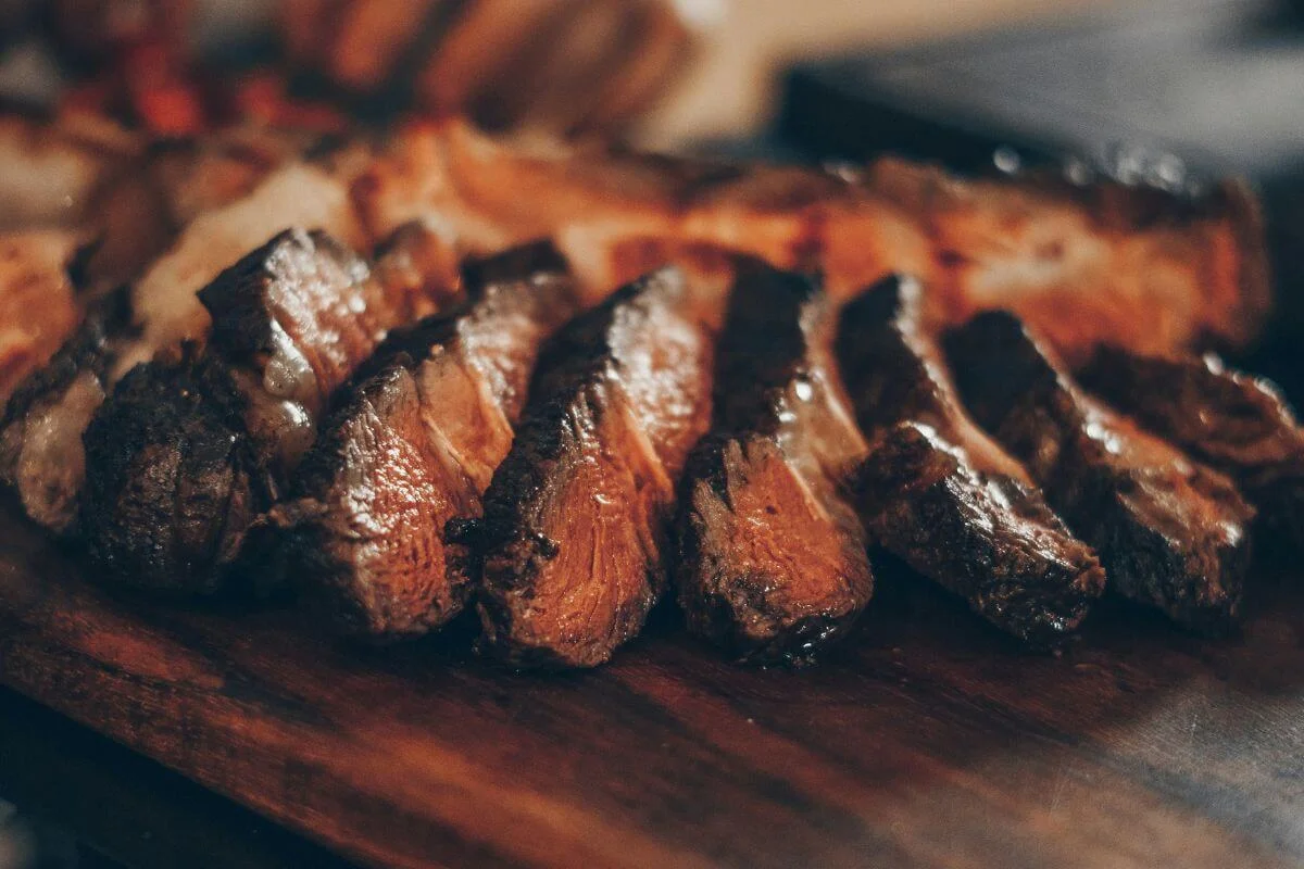 Close-up of sliced grilled steak with charred edges and juicy interior served on a wooden cutting board in a restaurant setting