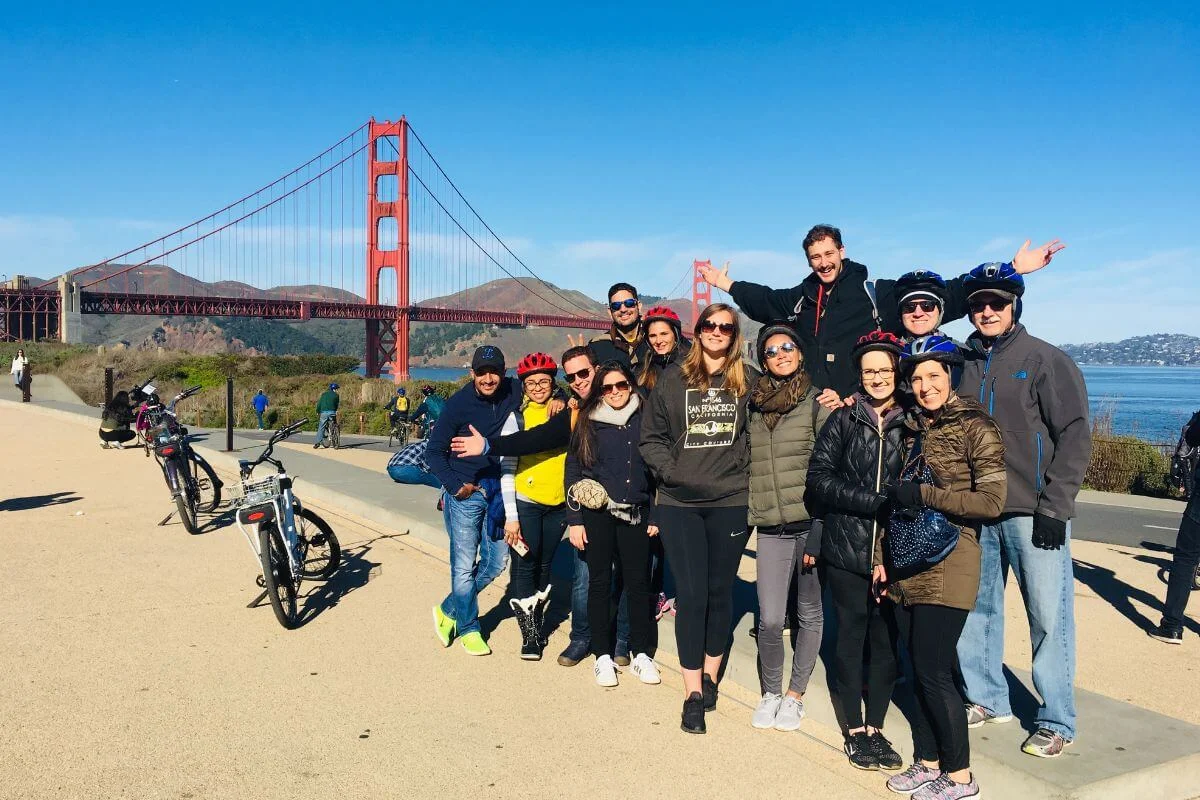 Group of tourists wearing helmets posing with bicycles near the Golden Gate Bridge during a guided bike tour in San Francisco.
