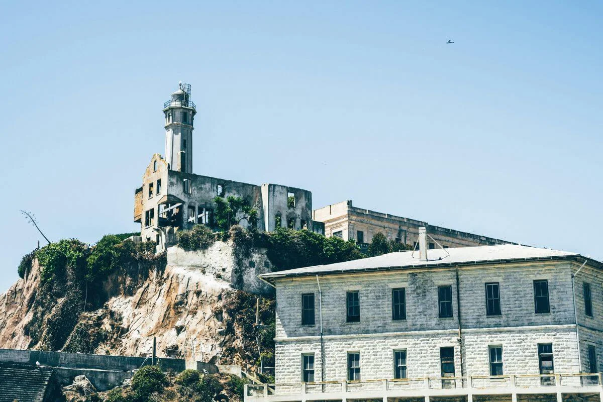 A close view of Alcatraz Island featuring the lighthouse and old prison structures perched on rocky cliffs overlooking the water under a clear sky.
