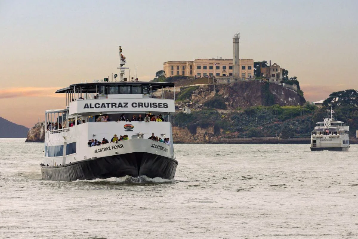 A ferry labeled “Alcatraz Cruises” carrying passengers across the water toward Alcatraz Island, with the historic prison and lighthouse visible in the background.