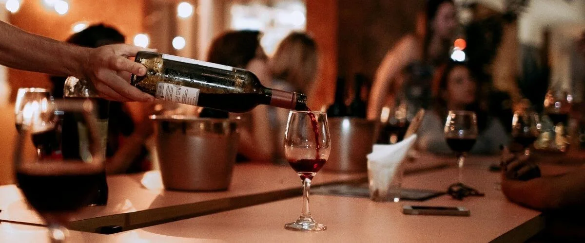 Evening Wine Service at Lamangata Resort A staff member pouring red wine into a glass at a warmly lit restaurant table while guests enjoy dinner in the background, creating an intimate evening dining atmosphere at a resort.