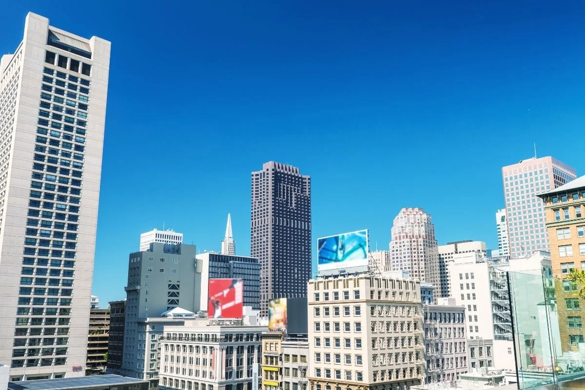 A clear daytime view of downtown San Francisco featuring modern high-rise buildings and city streets under a bright blue sky.