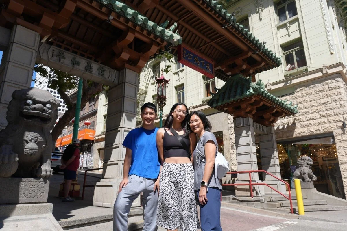 Three visitors posing in front of a traditional Chinese gate with stone lion statues in San Francisco’s Chinatown.