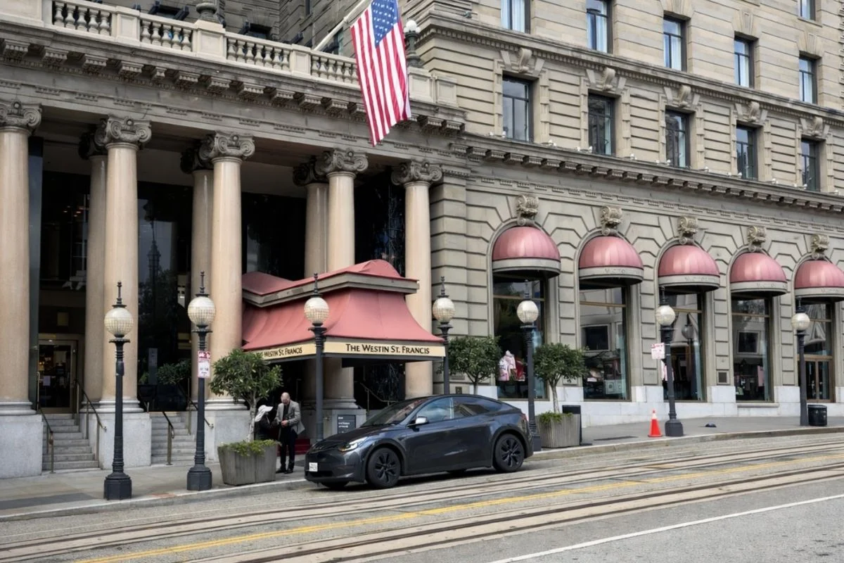 The entrance of The Westin St. Francis Hotel in San Francisco featuring classic architecture, American flag, red awnings, and a car parked along the street.