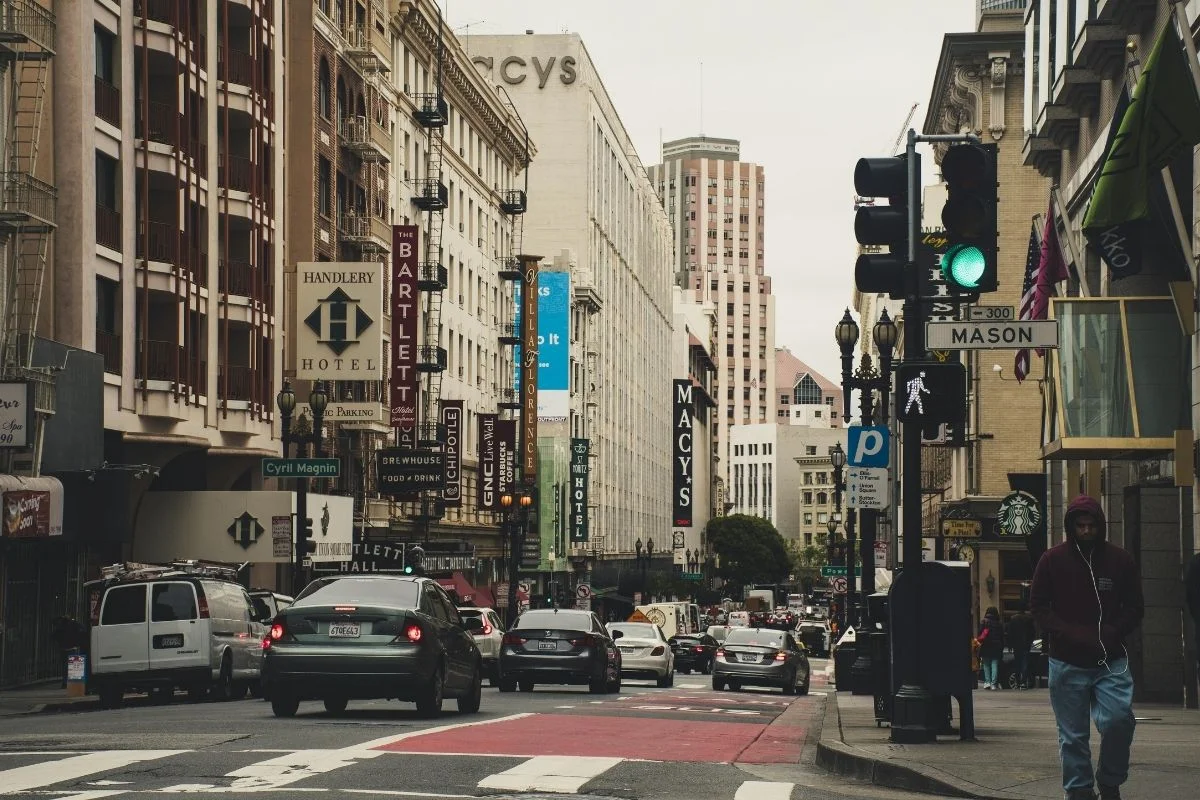 Busy downtown San Francisco street with cars, pedestrians, and storefronts including Macy’s and hotels near Union Square.