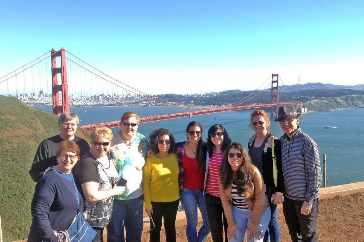 Group of tourists posing together with the Golden Gate Bridge and San Francisco Bay in the background on a sunny day.