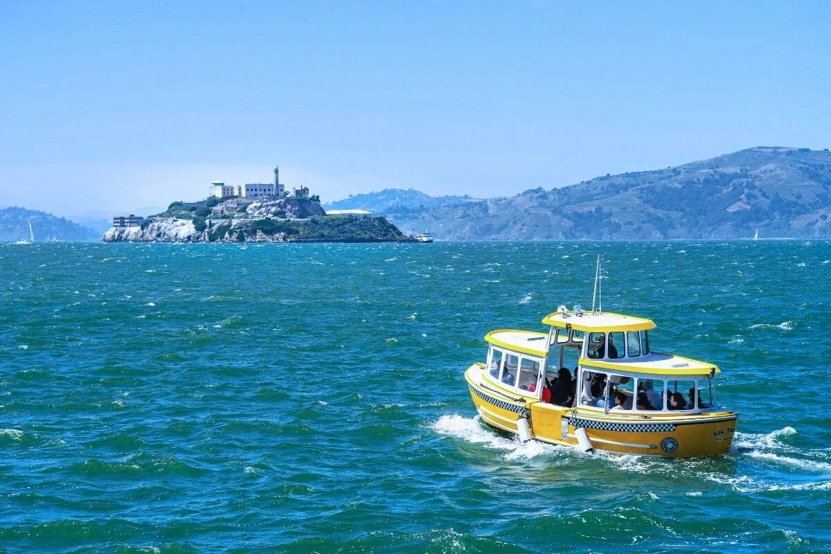 Small yellow boat cruising across San Francisco Bay with Alcatraz Island and its historic prison visible in the distance.