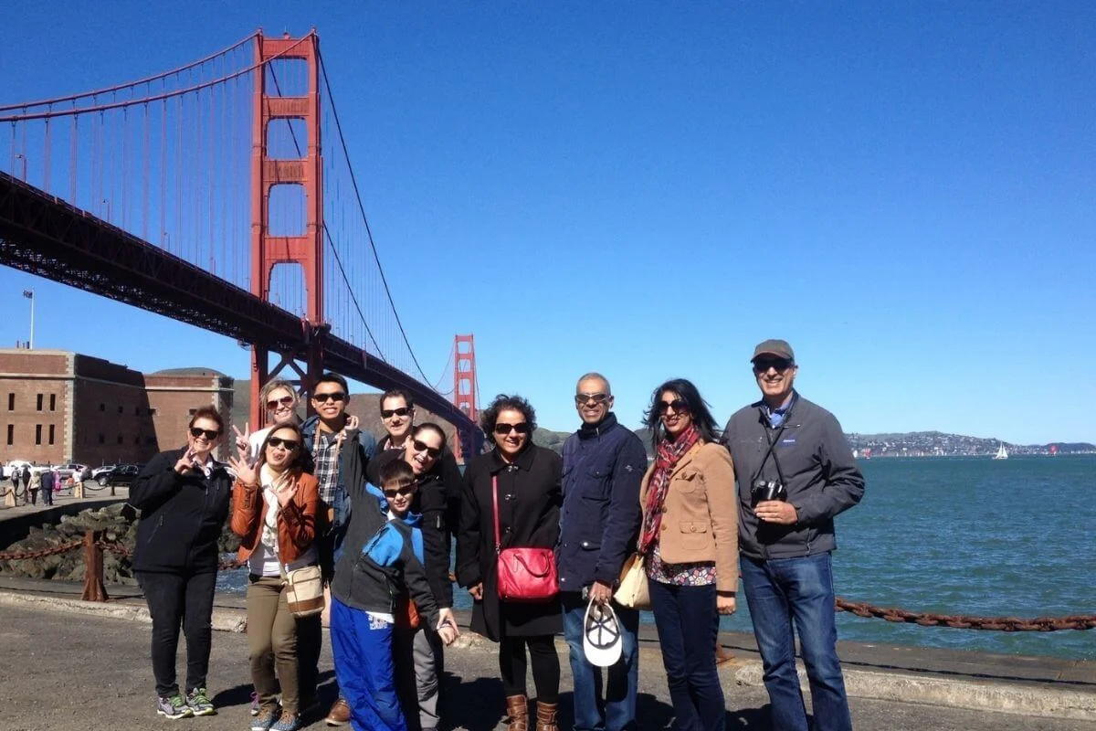 Group of tourists posing together near the Golden Gate Bridge with the iconic red suspension bridge and San Francisco Bay in the background.