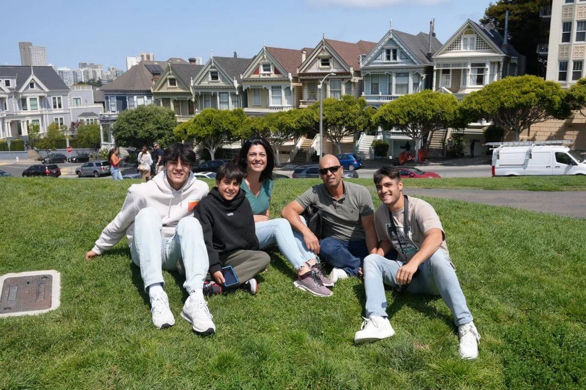 Group of visitors sitting on the grass at Alamo Square Park with the Painted Ladies Victorian houses in the background in San Francisco.