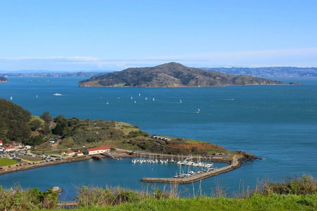 Scenic view of San Francisco Bay featuring Treasure Island in the distance, sailboats on the water, and a small marina along the shoreline.