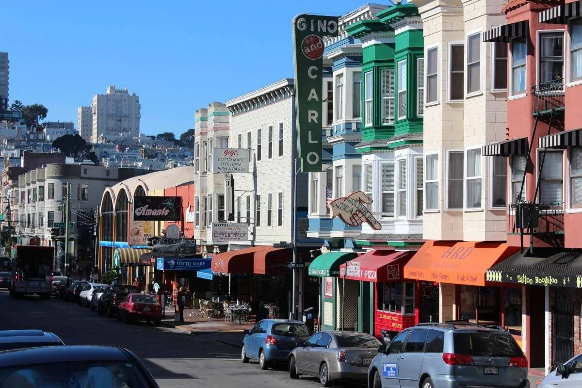 Vibrant San Francisco neighborhood street lined with colorful buildings, restaurants, and parked cars under a clear blue sky.