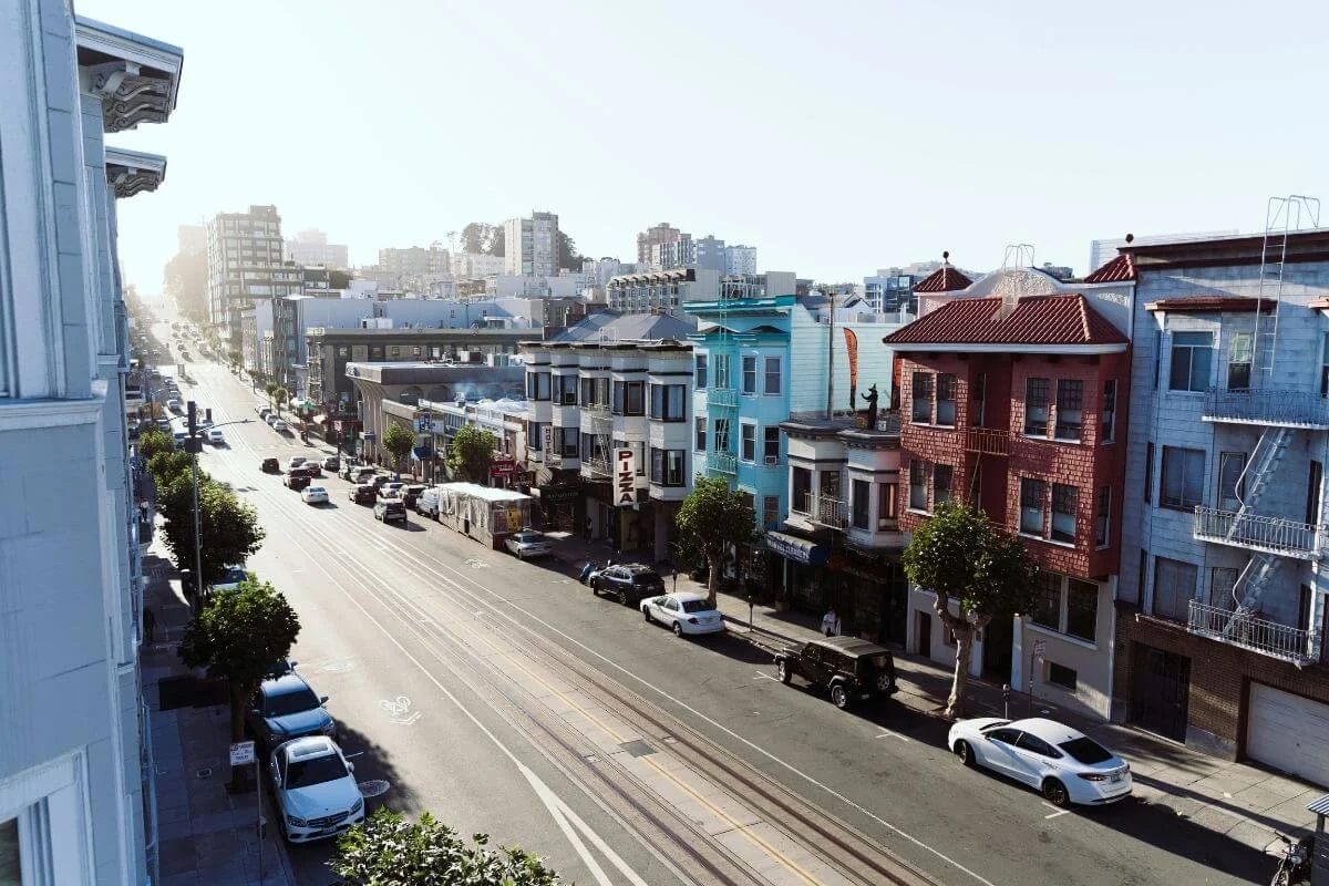 Scenic view of Nob Hill in San Francisco featuring colorful residential buildings, parked cars, and a sunlit city street.