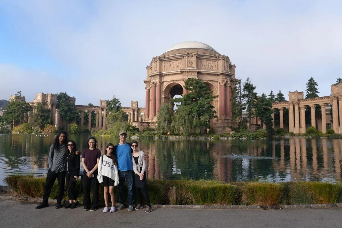 Group of visitors posing in front of the Palace of Fine Arts lagoon and classical rotunda in San Francisco on a calm day.