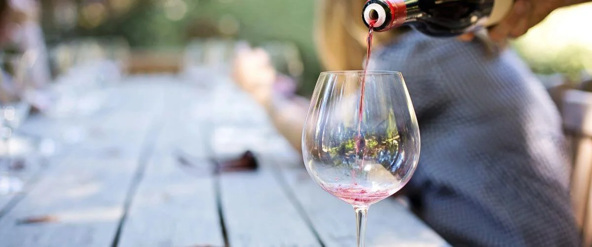 Red Wine Being Poured into a Glass During an Outdoor Wine Tasting A close-up of red wine being poured from a bottle into a large wine glass at an outdoor table during a wine tasting
